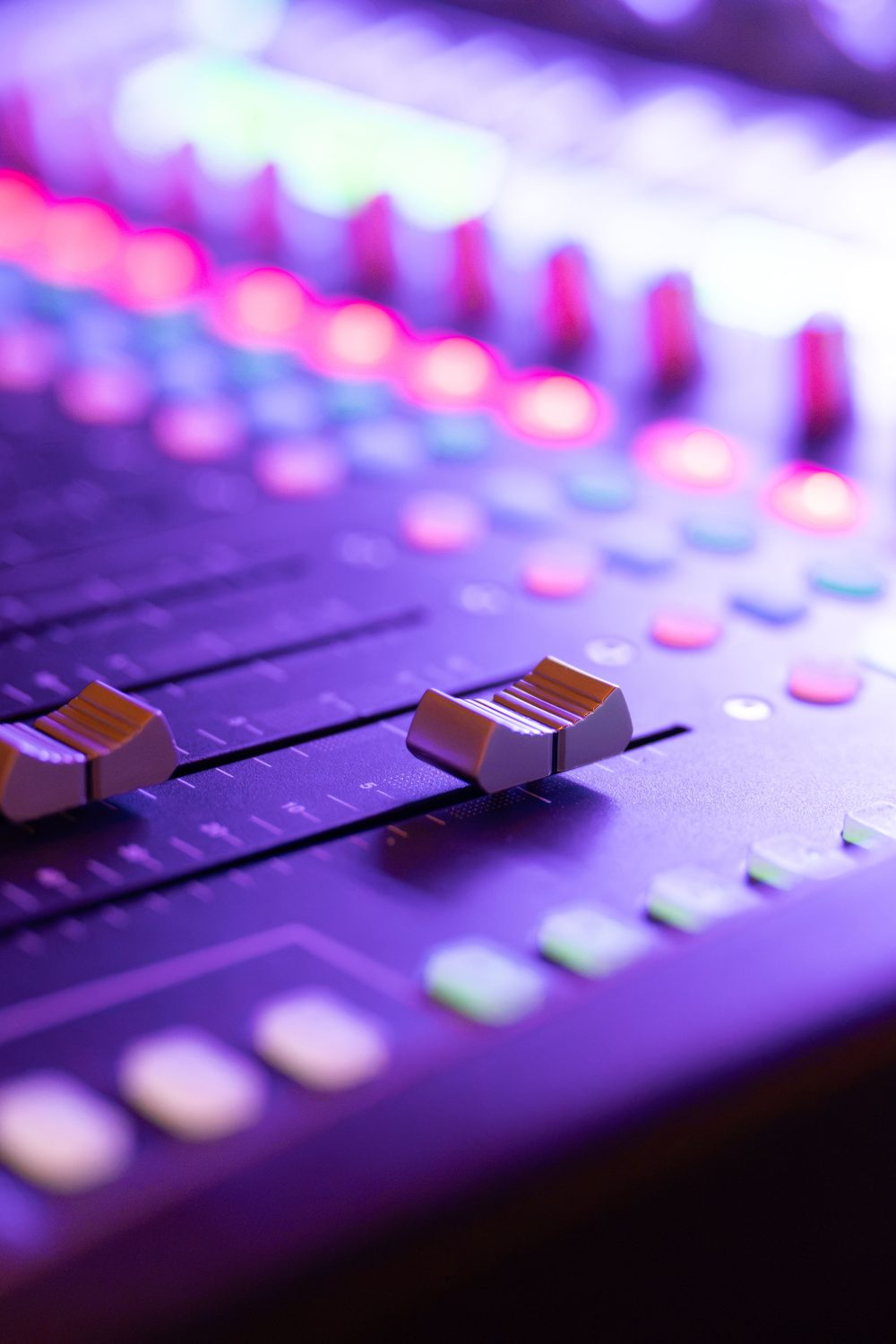 Close-up of mixing console faders under purple light